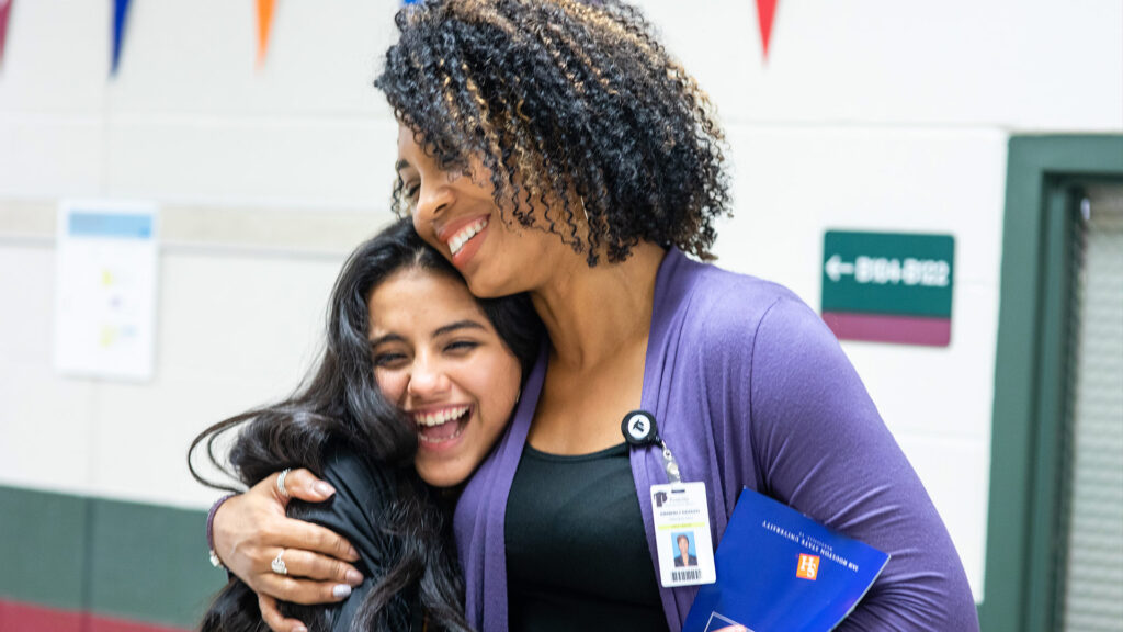 A principal gives a warm side-hug to one of her students in the school hallway.
