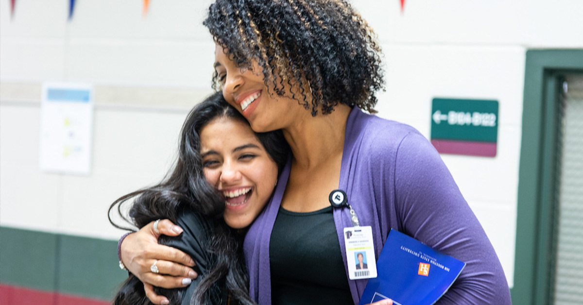 A principal gives a warm side-hug to one of her students in the school hallway.