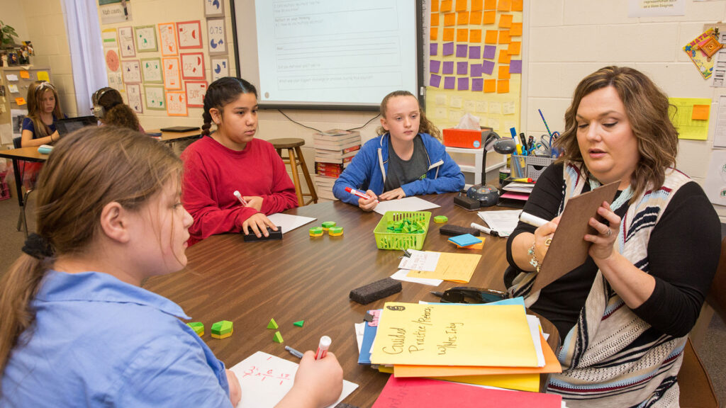 A middle school teacher in Cisco ISD works with three students on multiplying and dividing fractions at the teacher table