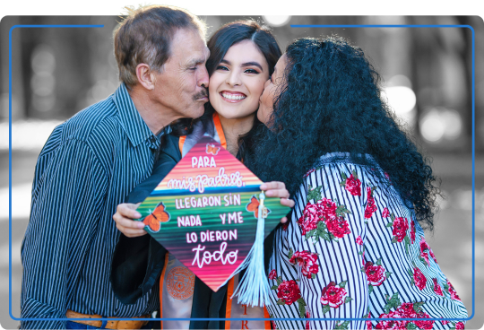 A graduate, Raquel Perez, is being kissed by both her parents.