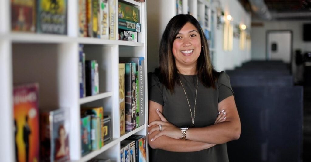 Voices on teaching video series features Erika Ramos. Erika is seen leaning against a nicely arranged bookshelf.