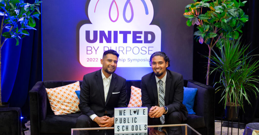 Victor Rios and Juan Terrazas pose at the 2022 leadership symposium against the United by Purpose logo backdrop.
