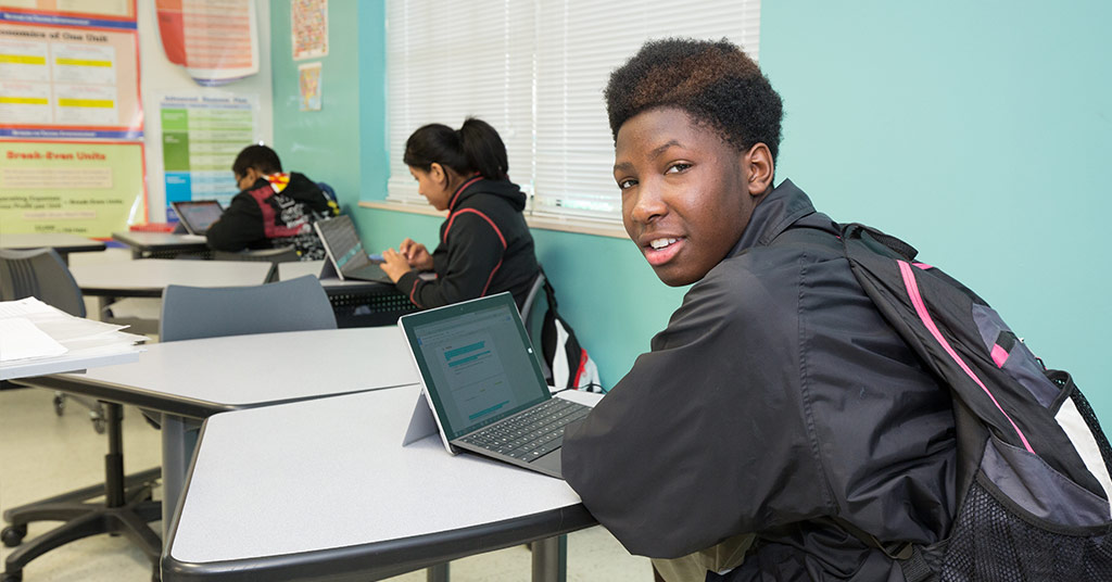 A student working on his laptop smiles for the camera.