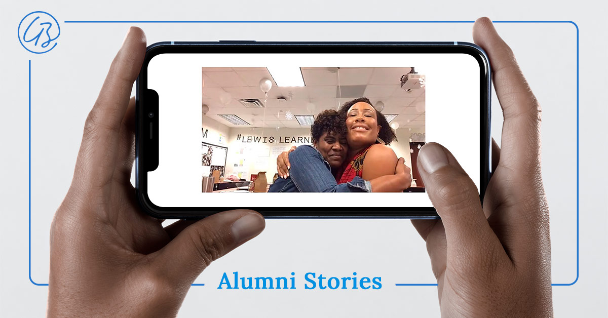 Two hands hold a cell phone as if recording a video. On the screen is an image of two educators who are colleagues giving one another a loving hug.