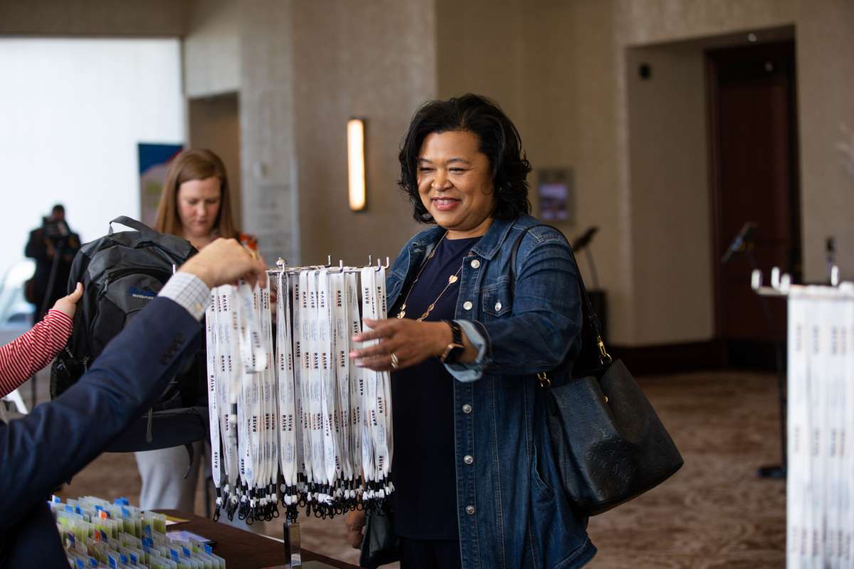Woman smiles as she reaches for her lanyard name tag at an event registration table.