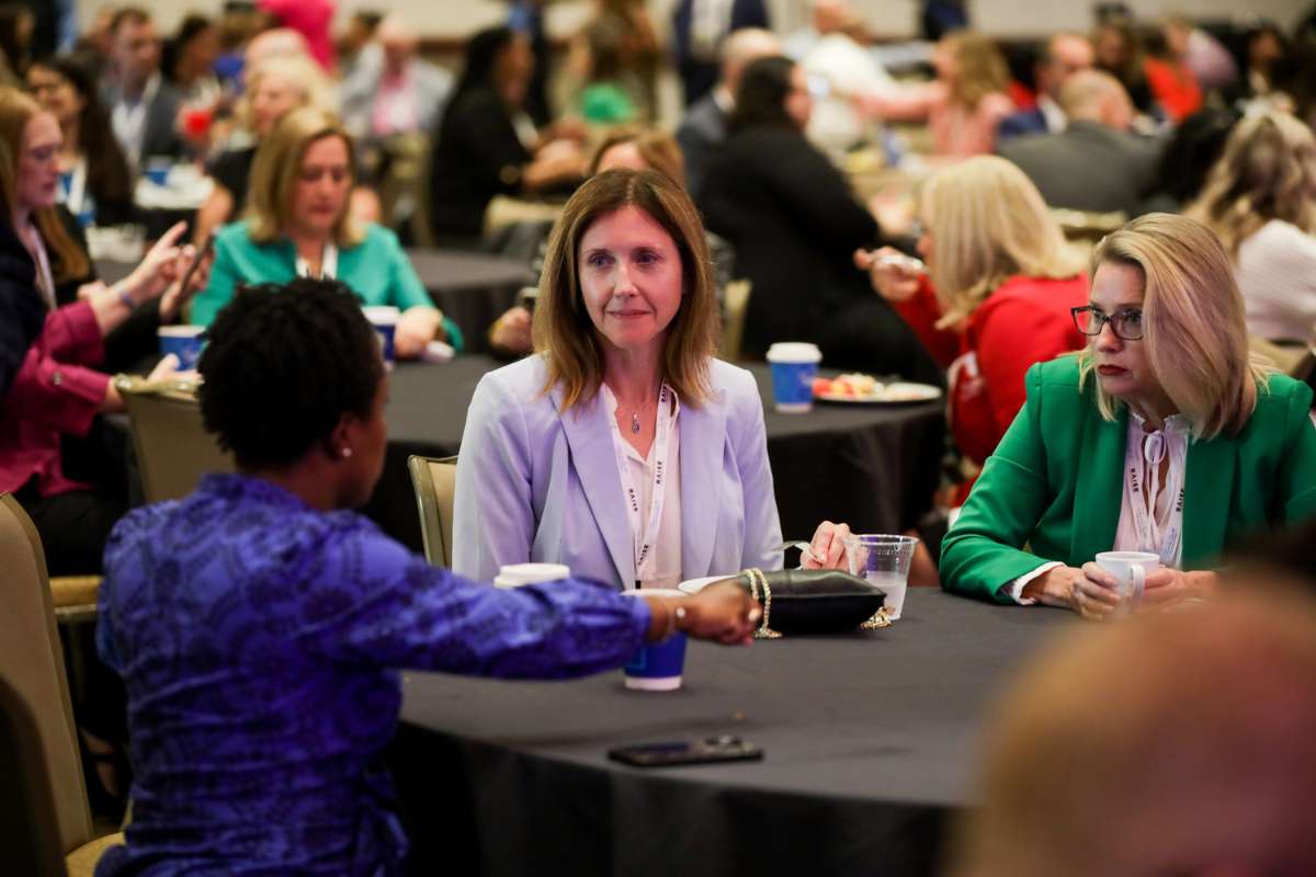 Three educators sit at a table in a large conference ballroom setting as they engage in discussion with one another.