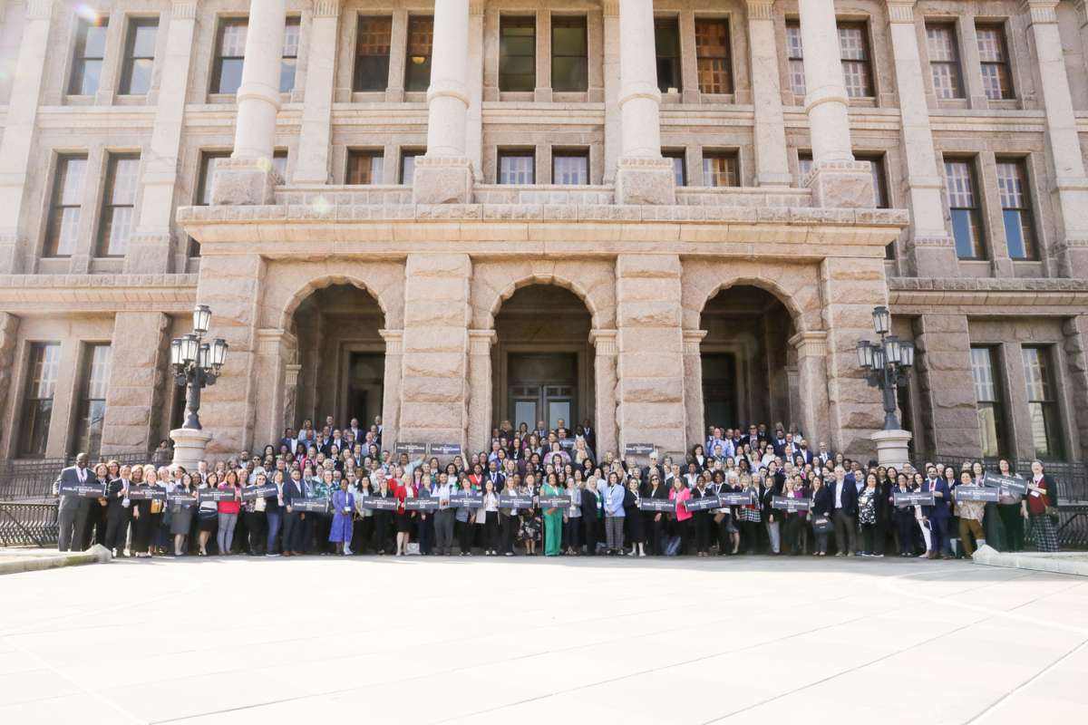 A large group of educators and school leaders smile as they stand together in front of the Texas Capitol. The front row of people are holding signs that read I advocated for public education today! with a Raise Your Hand Texas logo.