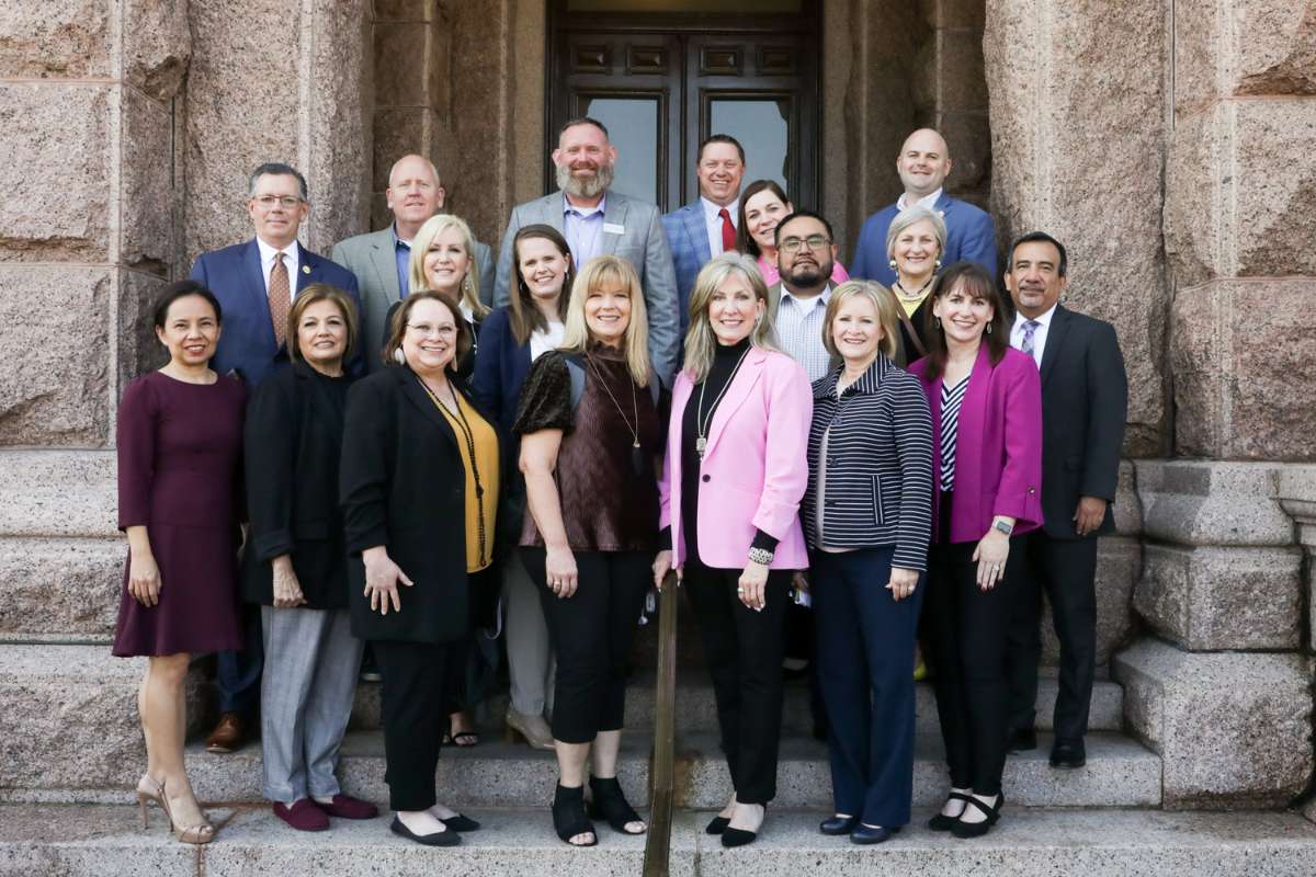 18 educators stand together on the steps of the Texas Capitol smiling looking straight forward.