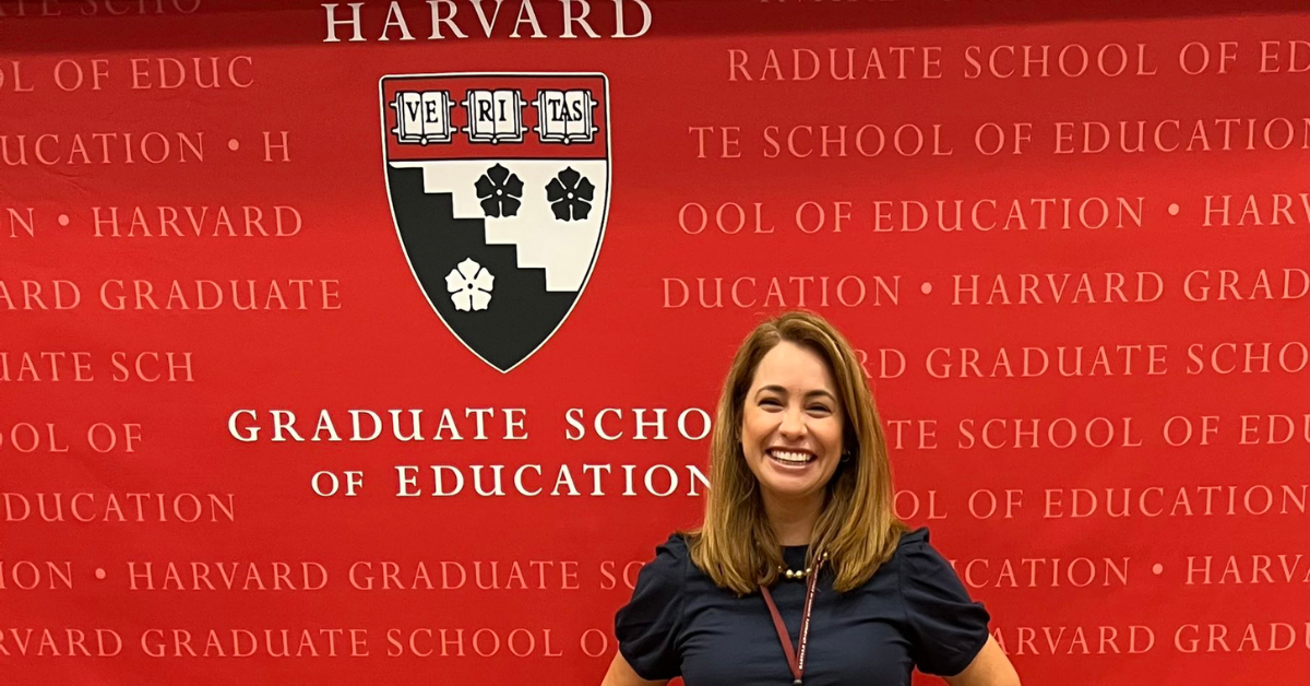 Nadia De La Rosa smiles while posing against the Harvard Graduate School of Education step and repeat backdrop.