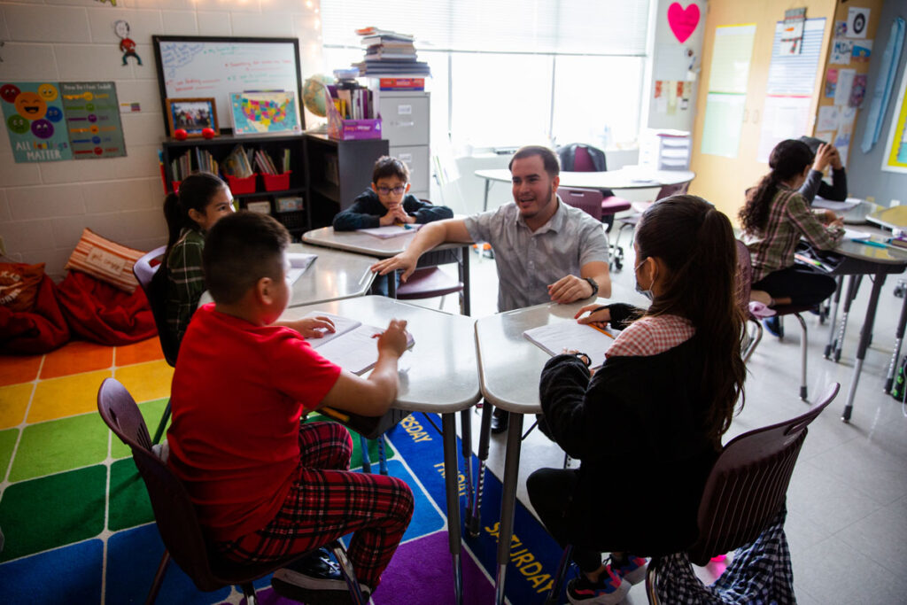 Fourth-grade teacher Uriel Iglesias kneels to talk with a small group of students about their lesson.