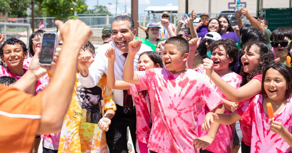 Dr. Jaime Aquino, San Antonio ISD Superintendent, standing with a group of children all smiling and celebrating