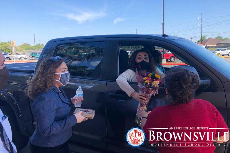 A parent leans out of a truck window to hand flowers to teachers in a Teacher Appreciation Day parade.