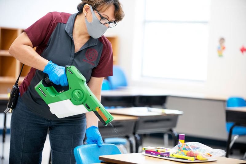 A staff member disinfects the tables of a classroom.