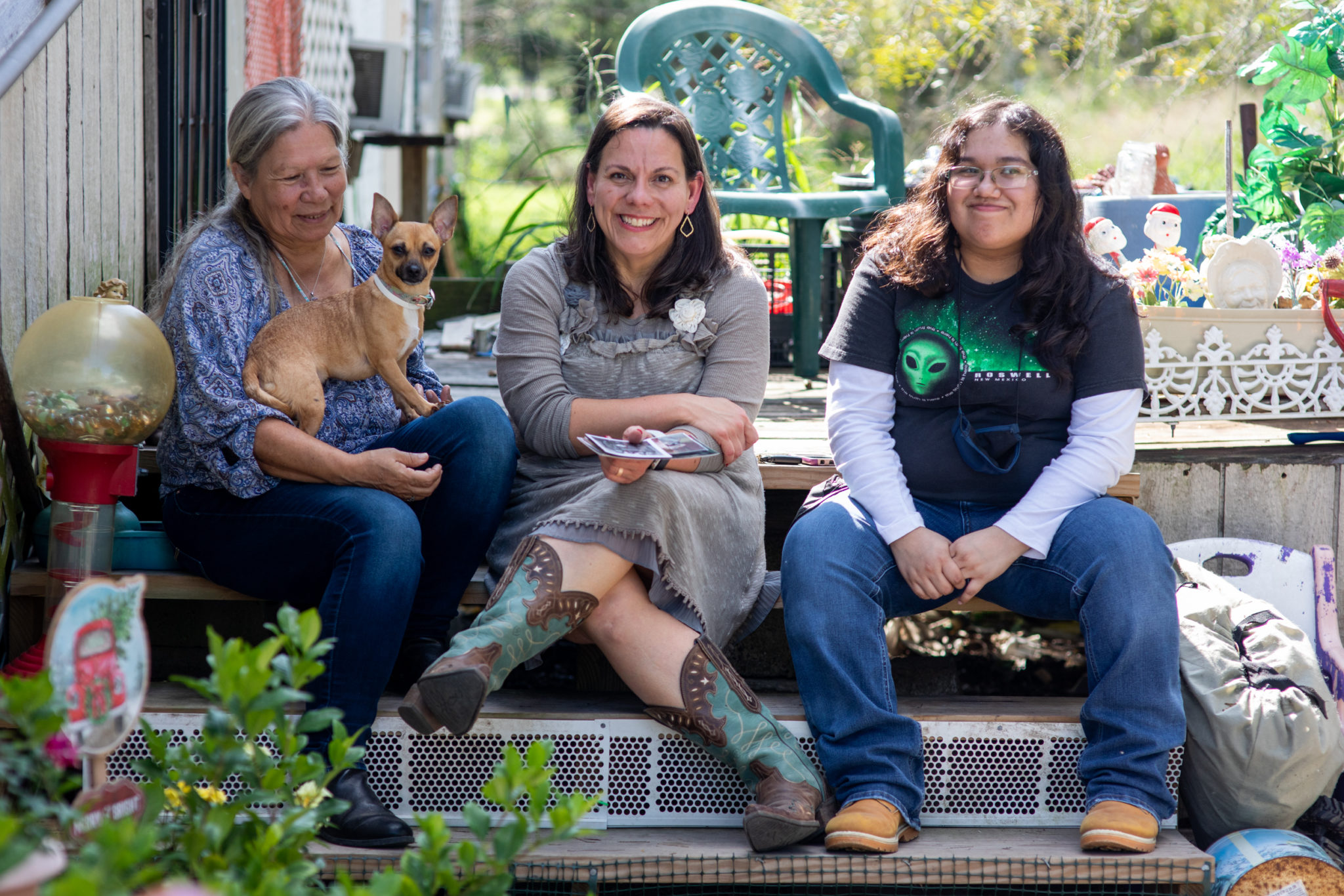 Natalia Goméz Ramback revisits the family home where she was raised. She sits on the porch with her sister Martha (left), niece Angelica (right), and Pearl the chihuahua who are the current stewards of the land and home.