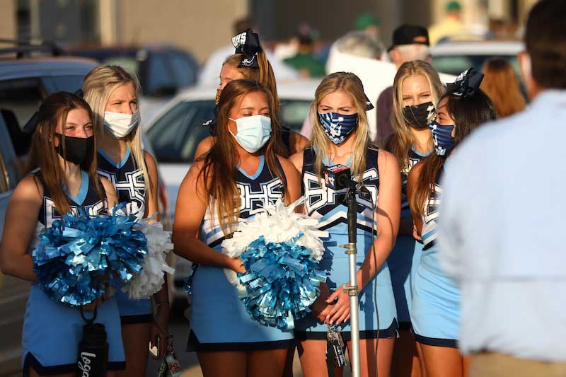 A group of seven cheerleaders gather together, they are all wearing masks.