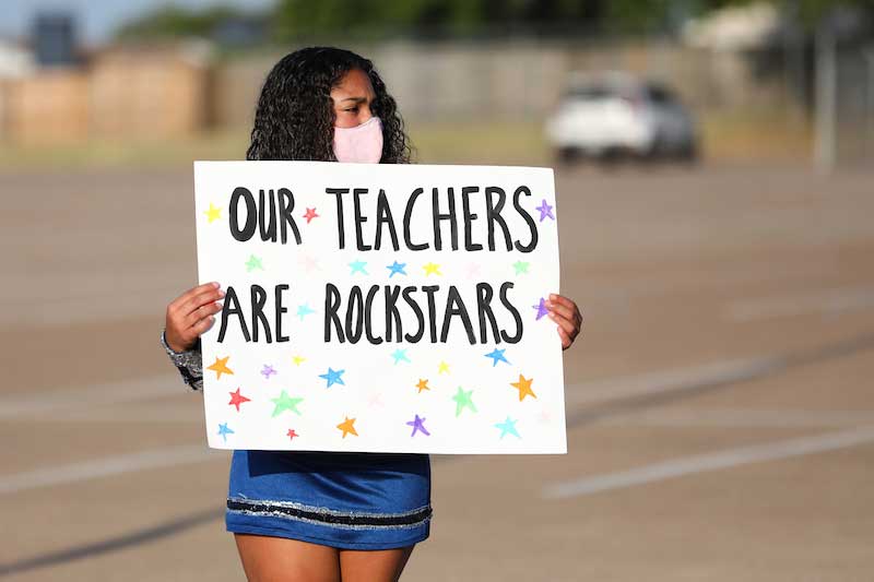 A cheerleader holds up a sign that reads "Our Teachers Are Rockstars."