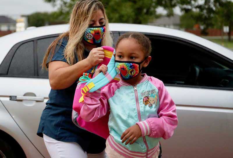 A parent helps her daughter into her backpack at drop off. Both are masked.