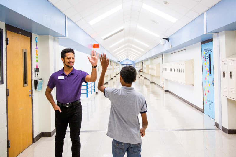 Trey high fives a student as they pass in the hallway.