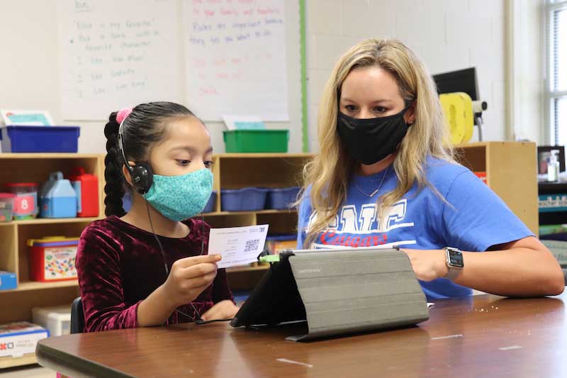 A teacher and student work together on a lesson. Both are masked. 