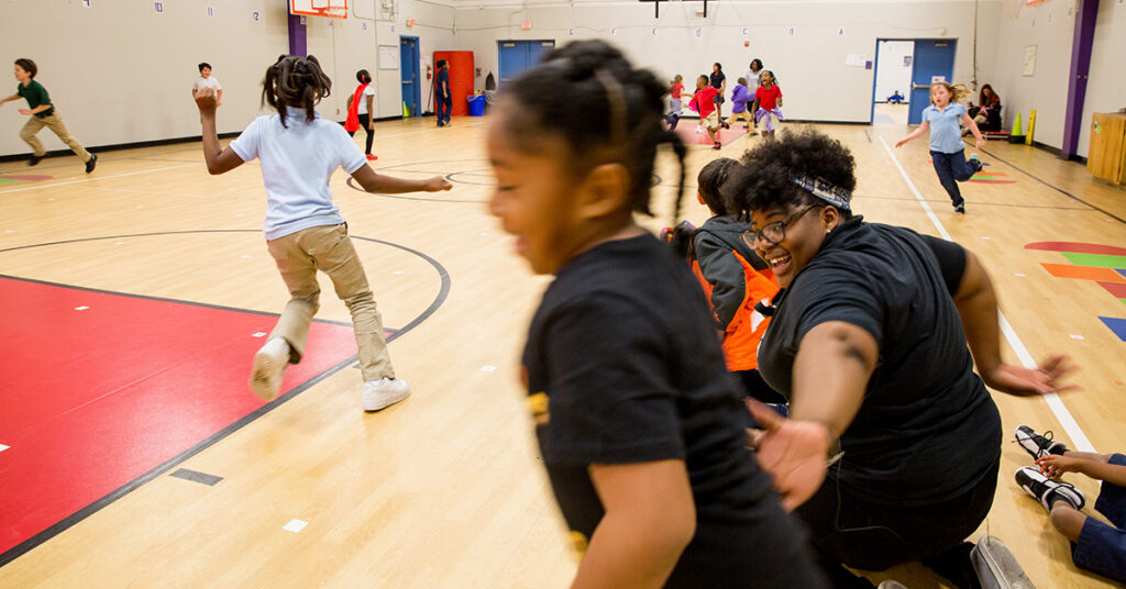 Students run around a school gymnasium in active game of freeze tag. In the midst of it all is Sherica – beaming.