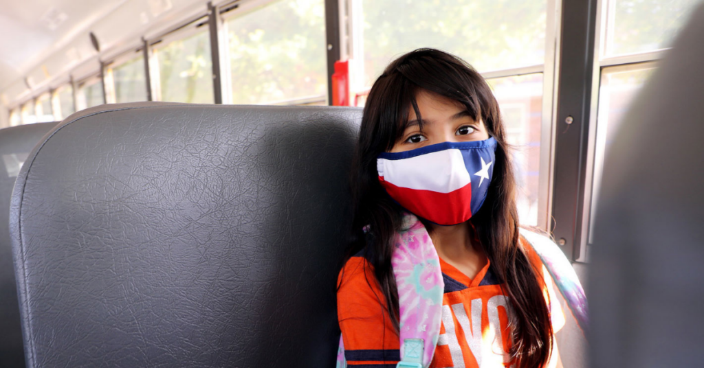 Child masked in a school bus. The design of the mask is the Texas flag.