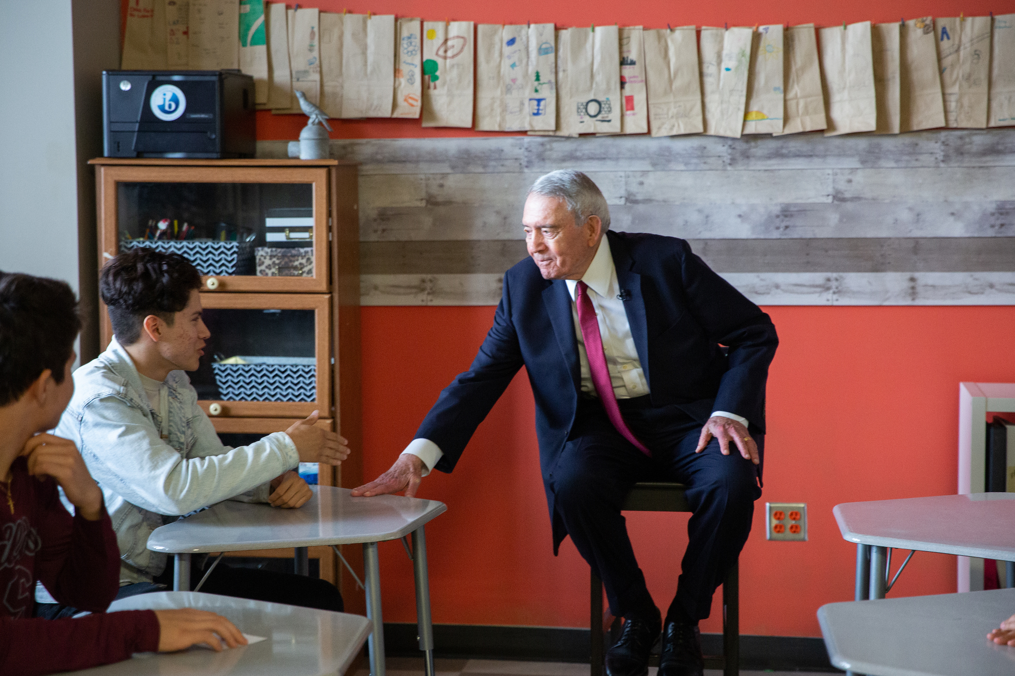 Legendary News Anchor Dan Rather meets with students at his alma mater in Houston ISD. He poses questions to the current student body about the importance of public schools. In this photo he leans closer to the desk of a student to better hear hear their thoughts.