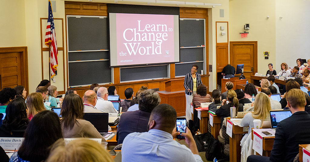 Dr. Karen Mapp, a senior lecturer at the Harvard Graduate School of Education stands at the front of a full lecture hall with a welcoming smile on her face. The screen behind her reads "Learn to Change the World."